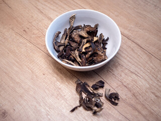 Dried bolete mushrooms in a light brown bowl on a wooden table. Natural dehydrated wild mushrooms prepared for cooking and seasoning.