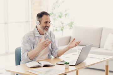 Mature businessman working remotely in a modern home office with a laptop, headset, and notes, illustrating a productive lifestyle