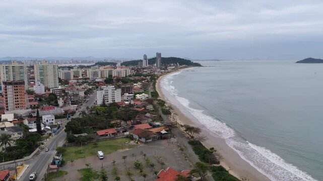 rom a low drone view, Penha&rsquo;s coast reveals Praia do Trapiche and Praia de Arma&ccedil;&atilde;o, with red-roof homes, beachfront towers, and forested hills rising behind the Atlantic shoreline.