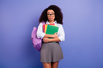 Cute female student holding notebooks and backpack in thoughtful expression on purple background wearing a school outfit