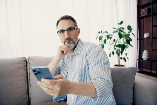 Professional man with glasses using a smartphone at home interior setting, showcasing a stylish modern lifestyle