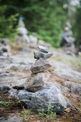 A close-up view shows a carefully stacked cairn of grey stones standing on a rocky surface in the woods