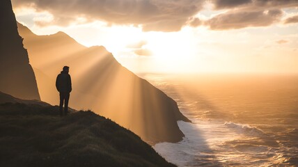 Silhouette of a person standing on a cliff overlooking the ocean at sunset, with sun rays shining through the clouds and illuminating the water and the coastline