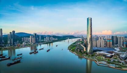 Aerial view of a modern city skyline with a prominent skyscraper tower and commercial barges on the river in Zhuhai.