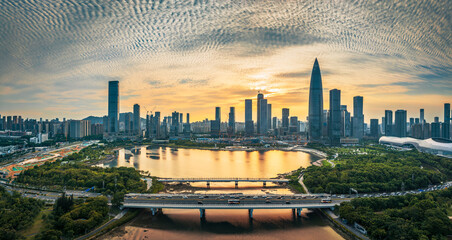 Aerial view of a modern city skyline with a bridge and traffic over a river during a beautiful golden sunset in Shenzhen.