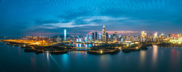 Panorama of a modern financial district skyline with city lights reflecting on the water surface at night in Shenzhen, China.
