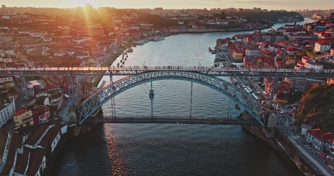 Portugal, Porto: Colorful sunset over Dom Luis I Bridge spans Douro river at golden hour, people walking upper deck, bright historic riverside cityscape buildings. Aerial view drone footage landscape