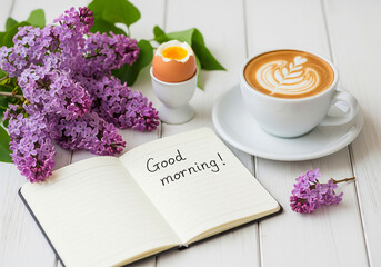 Good morning" concept with a cup of coffee, a handwritten note, and fresh lilac flowers. Cheerful spring breakfast still life on a white wooden table.