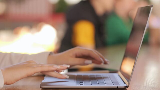 Woman is typing on a laptop. The laptop is open and the screen is black. The woman is wearing a white shirt