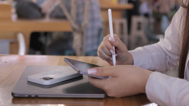 Woman is holding a white pen and a cell phone. She is sitting at a table