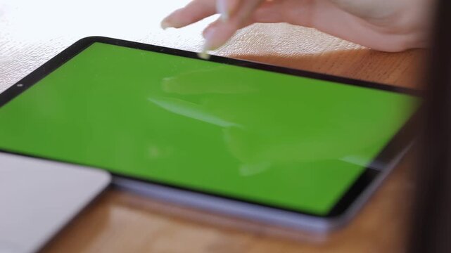 Woman is using a tablet with a green screen. She is touching the screen with a pen