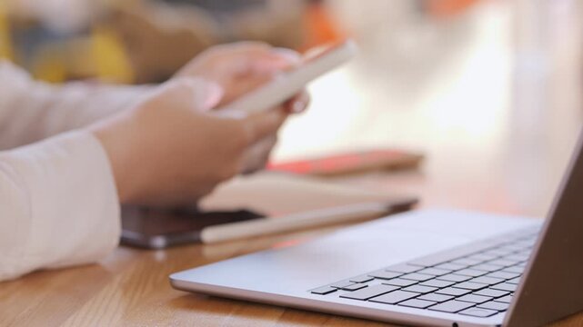 Woman is sitting at a table with a laptop and a cell phone. She is holding the cell phone in her hand