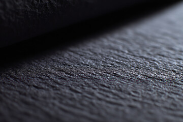 Close-up of a textured black surface with subtle lighting, highlighting roughness and fine details in a shallow depth of field
