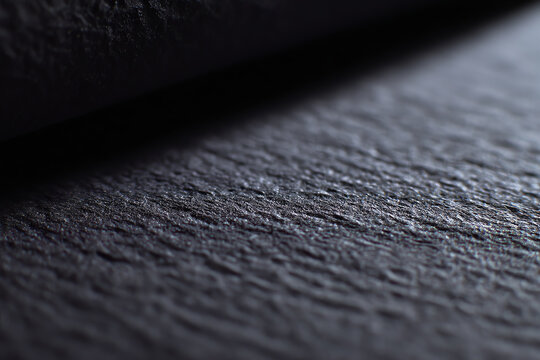 Close-up of a textured black surface with subtle lighting, highlighting roughness and fine details in a shallow depth of field