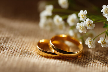 Two gold wedding rings rest on textured fabric alongside delicate white baby's breath flowers, symbolizing love and commitment in a warm, intimate setting