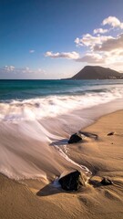 Ocean Waves Crashing on Sandy Beach with Mountain Background