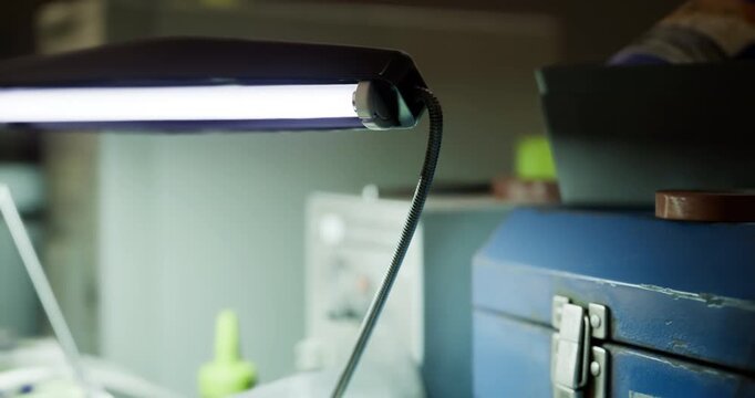 Colorful tools and supplies are scattered across a cluttered workspace, illuminated by a bright lamp. Scissors, tubes, and containers create a lively atmosphere for creativity.
