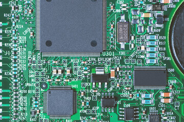 Macro close-up of a green circuit board from an old hard disk drive. Visible microchips, resistors, and solder joints show detailed electronic components and vintage technology.