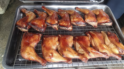 Smoked roasted duck leg quarter on metal rack, savory golden glaze and crispy skin, appetizing outdoor barbecue presentation