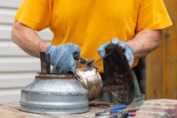 A man wearing gloves uses metal shears to cut a chimney cap. A man repairs a chimney cap.