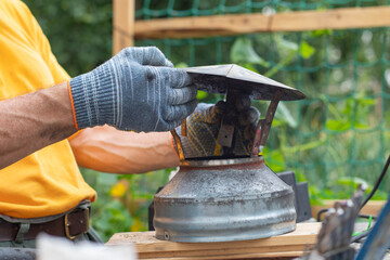 A man wearing gray work gloves holds a chimney cap in his hands.