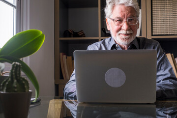 Senior man working on laptop at home in a home office, calm and smiling, symbol of professional...