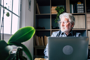 Fototapeta premium Senior man working on laptop at home in a home office, calm and smiling, symbol of professional life, remote work, digital skills, modern lifestyle and confident aging, productivity and focus