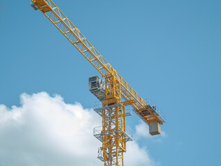 Naklejka premium Equipment for the construction and lifting of bulky goods with construction materials. A tower crane on a construction site against a rainy sky. A construction high-rise crane and leaves on a tree.