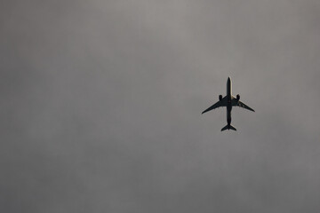 Silhouette Of A Passenger Airplane Flying High In A Grey, Moody And Overcast Sky. Travel And Aviation Concept With Copy Space.