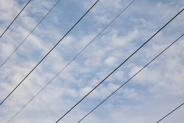 An Abstract View Of Several Electrical Wires (Power Lines) Crossing Diagonally Against A Blue Sky With White Clouds.