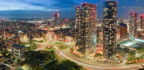 Blue-hour panorama of Manchester skyline with Deansgate Towers and glowing traffic trails at Mancunian Way roundabout. 