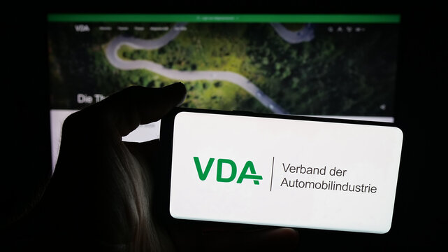 Stuttgart, Germany - 10-06-2025: Person holding mobile phone with logo of German Verband der Automobilindustrie (VDA) on screen in front of web page. Focus on phone display.