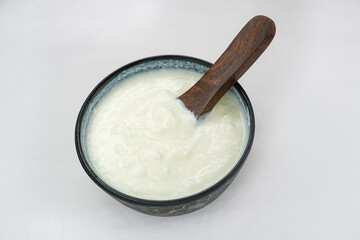 Homemade dahi doi or sour cream or curd or yogurt in brown earthen pot with wooden spoon on white background. Curdled milk. Probiotic food or Probiotic dairy product.