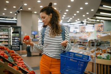 Woman choosing fresh tomatoes from the produce section in a grocery store, shopping for healthy food and picking organic vegetables to prepare nutritious meals