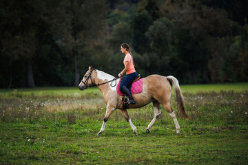 Recreational horseback riding in rural pasture. Woman enjoying riding her paint horse outdoors