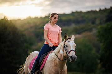 Woman riding horse during equestrian training session at sunset. Female rider practicing horseback riding