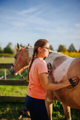 Woman rancher brushing horse at paddock. Female animal groomer take care of paint horse at farm