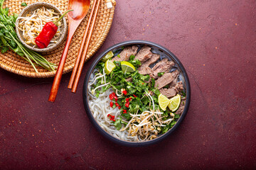 Pho Bo Vietnamese soup, bowl of fresh asian soup with rice noodle, beef meat, herbs, soy sprouts and chili on red background, top view. Asian cuisine, comfort food.