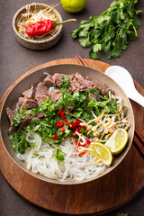 Pho Bo Vietnamese soup, bowl of fresh asian soup with rice noodle, beef meat, herbs, soy sprouts and chili on dark background, vertical photo. Asian cuisine, comfort food.