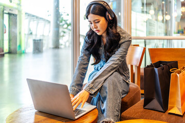 Obraz premium Young asian woman working or studying online with laptop and headphones, showing digital lifestyle, e-learning, remote work, freelance work digital nomad, shopping online, modern tech Wi-Fi at cafe
