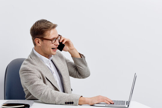 smiling caucasian man use laptop talk on phone remote work digital nomad online communication cheerful business casual outfit modern office interior