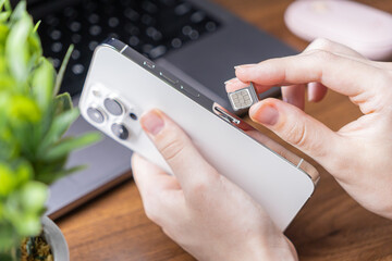 Person installing new micro SIM card into modern white smartphone, enabling essential mobile...