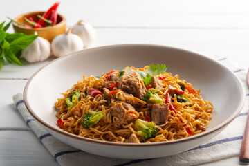 Spicy stir fried instant noodle with canned tuna fish broccoli and thai basil leaves in white plate.