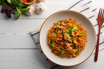 Spicy stir fried instant noodle with canned tuna fish broccoli and thai basil leaves in white plate.Top view.