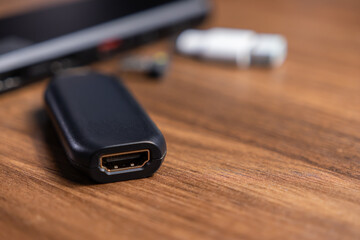 Black HDMI adapter with visible port resting on a wooden desk, representing modern digital connectivity and display solutions for home or office