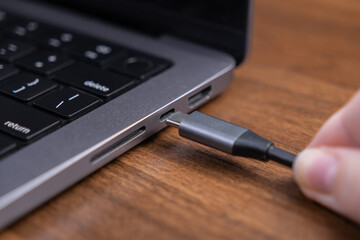 A hand plugs a universal USB-C cable into a modern laptop's port on a wooden desk, showcasing essential digital technology for efficient data and power