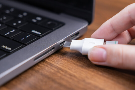Close-up of human hand meticulously inserting a universal white USB-C cable into a contemporary gray laptop port, symbolizing versatile digital connectivity, data exchange, and power