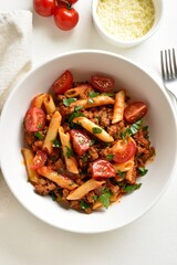Bowl of bolognese penne pasta with minced meat, tomatoes and gre