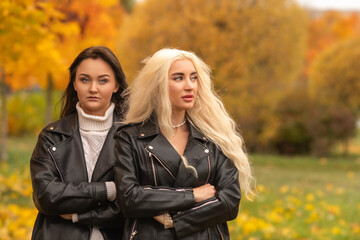 Two women with contrasting hairstyles and stylish leather jackets pose back to back in a vibrant...