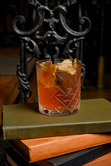 Orange alcoholic cocktail with ice on a stack of old books and dark background.